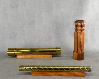 A brass spiral kaleidoscope, 12-1/2" length, on a small wooden display stand; a handcrafted, hand-turned zebrawood barrel kaleidescope approximately 9-1/2" tall, and a large brass cylindrical kaleidoscope with wooden stand, approximately 14" long.