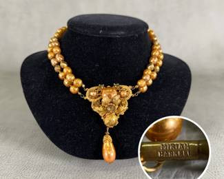 A vintage signed Miriam Haskell statement necklace with two strands of glass-base baroque pearls with a lustrous, rich warm bronze or coppery-orange iridescent coating, interspersed with faceted metallic hematite-toned or brass-plated accent rondelles, suspending a highly detailed, triangular Art Nouveau-inspired statement pendant of textured, repoussé-style golden leaves and floral petals curling around larger baroque glass pearls, with one large baroque faux pearl dangle.  