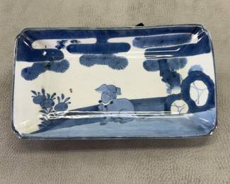 A Japanese Arita Ware porcelain blue and white tray, 19th century, rectangular tray with dimpled corners hand painted in cobalt blue featuring design of dog wearing a collar, sitting on a fenced terrace beneath pine trees; unmarked, 8-1/4” long by 4-3/4” wide by 1-1/2” high.