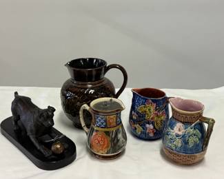 Collectibles including a vintage sculpture of a playful dog reaching for a small ball, crafted in the style of 19th-century animalier sculptors like Pierre-Jules Mêne; a vintage ceramic or ironstone pitcher featuring a dark marbled or slag-style glaze, accented with Japanese-inspired Imari floral motifs, gold gilding, and a fitted pewter lid; two small majolica pitchers, and a vintage dark brown Rockingham-glazed pottery pitcher