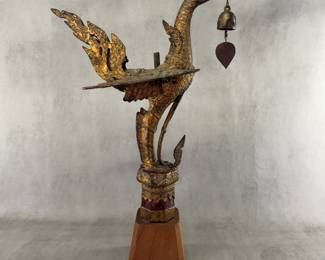 A Thai gilt temple bird sculpture, known as a Hong or Hamsa (a sacred swan or mythical goose in Thai-Buddhist mythology), holding a small wind bell in its mouth, and mounted on a wooden base. Gilded metal, 25-1/4 inches tall including the base.