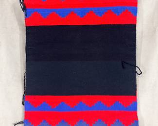 A traditional Navajo biil (also known as a rug dress or beele dress), featuring a black center field bordered by bands of blue and red stepped/zig-zag patterns. 22.5”W x 27.5”H.