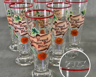 A set of eight vintage Pilsner Urquell glass pilsner flutes featuring a scroll label graphic, vine/leaf accents, a red rim, and an orange wax seal design reading "Gegr. 1842"