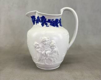 Rare antique Wedgwood "Bacchanalian Boys" pitcher, 7-1/2”H, white jasper, decorated with Classical imagery of young boys and satyrs in Bacchic revelry (with grapes and grape leaves in their hair.) On one side, a young Bacchus holding his thyrsus (fennel staff) is being held aloft by two other boys, a vessel of wine beside them; the other scene has a satyr and young Bacchus sitting beneath a tree. The neck of the pitcher has applied blue sprig band of fruiting grape vines. Marked with "WEDGWOOD" to the base, dating 1790 to 1820.