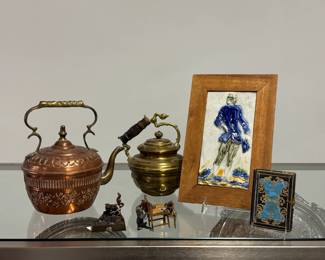 Vintage hand-hammered copper tea pot or kettle with brass spout, finial, and handle; a vintage solid brass tea kettle with a curved handle and a ribbed wood grip; a mid-century Italian ceramic or majolica bas-relief tile framed in wood