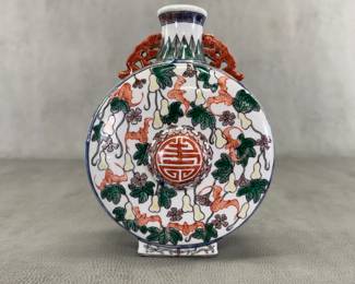 A vintage Chinese porcelain polychrome enamel moonflask vase, 9 inches tall, featuring hand-painted designs of flying bats and fruiting gourd vines, with a central medallion displaying a Shou character—a traditional symbol meaning longevity and long life. Two molded, coral-red iron-red chilong (hornless mythical dragons) anchor the neck to the shoulders. 
