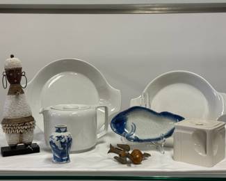 A hand-carved Namji (or Namchi) fertility doll from Cameroon, decorated with white seed beads and cowrie shells; two Helios fireproof ceramic two-handled dishes made in Germany; a modern replica porcelain Cube Teapot, a vintage Seltmann Weiden white glazed teapot with minimalist, cylindrical design featuring a recessed flat lid and a prominent square geometric handle, made in Bavaria, West Germany; a vintage Japanese blue and white porcelain fish-shaped dish, and an antique Victorian brass sewing bird clamp equipped with a built-in pin cushion