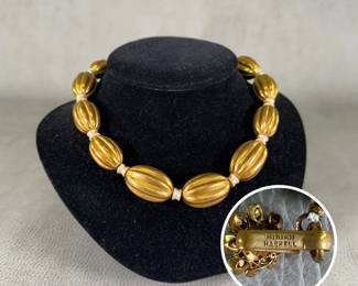 A mid-century vintage Miriam Haskell ribbed melon bead choker necklace featuring large, elongated gold-tone barrel beads with a textured fluted or ribbed pattern, separated by delicate ivory-colored spacer beads. Gold-toned clasp stamped with the text "MIRIAM HASKELL"