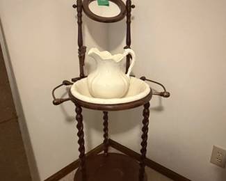 Washstand with three barley-twist legs, a round lower shelf, mirror, candlestick holders, and a basin and ruffled pitcher.