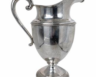 Elegant sterling silver footed water pitcher or ewer featuring a classic baluster-form body, broad sweeping pour spout, raised circular pedestal base, and graceful open scroll handle with curled terminal. The polished sterling surface displays subtle engraved decoration to the body and an impressive traditional silhouette. A substantial decorative and functional piece suitable for serving, display, or inclusion in a sterling silver collection. Pre-owned condition with visible surface scratching, tarnish/patina, spotting and other signs of age and use. Please review photographs carefully for condition and details. Sterling silver; maker and exact age to be determined from hallmarks.