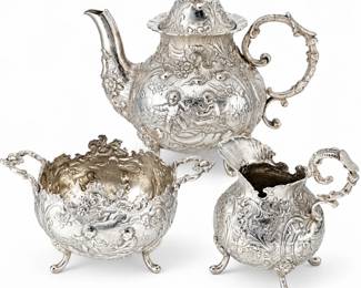 Antique German .800 silver three-piece tea service featuring a teapot, covered sugar bowl, and creamer, each richly decorated in elaborate high-relief repoussé work with scrolling foliate motifs, floral details, figural scenes, ornate handles, and shaped feet. The teapot is topped with a decorative floral finial and the entire set displays the highly detailed craftsmanship associated with nineteenth- and early twentieth-century Continental silver. Marked 800 silver. A striking and highly decorative antique German silver service well suited for collectors of European silver, ornate tableware, Victorian-style décor, and fine decorative arts. Please review all photographs carefully for hallmarks, measurements, design details, and condition, as photographs are considered part of the description.