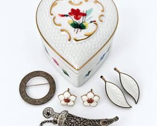 Charming vintage jewelry collection featuring an assortment of sterling silver and enamel brooches and earrings accompanied by a decorative heart-shaped porcelain trinket or jewelry box. The jewelry grouping includes a pair of white enamel floral earrings with warm rose-tone floral centers, a pair of elongated white enamel leaf-form earrings marked “925S,” a circular open-center brooch, and an ornate dimensional filigree scimitar or dagger-form brooch with safety chain. The heart-shaped porcelain box features a textured white ground with colorful hand-painted-style floral decoration and gilt accents. Jewelry displays varying degrees of vintage patina, oxidation and age-related surface wear, which have been left intact and not polished. An attractive estate collection combining vintage sterling silver jewelry, enamel work, filigree and decorative porcelain. Please review all photographs carefully for hallmarks, construction, enamel condition, patina and overall condition.