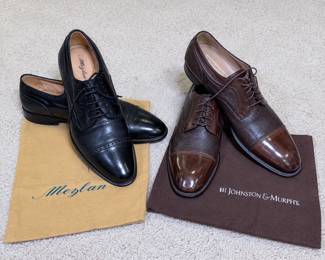 Collection of two pairs of quality men’s designer dress shoes featuring Mezlan and Johnston & Murphy Domani. Includes black Mezlan leather lace-up oxfords with polished cap toes and brogue detailing, accompanied by Mezlan shoe bags, and brown Johnston & Murphy Domani lace-up dress shoes featuring contrasting textured leather panels and polished cap toes, accompanied by a Johnston & Murphy shoe bag. Approximately men’s size 10 1/2; bidders should review photographs and interior markings for sizing and fit. Both pairs are pre-owned and show visible wear consistent with use, including creasing, surface marks/scuffs and wear to the soles. A handsome name-brand grouping of classic men’s business and formal footwear. Please review all photographs carefully for style, condition, markings and included accessories.