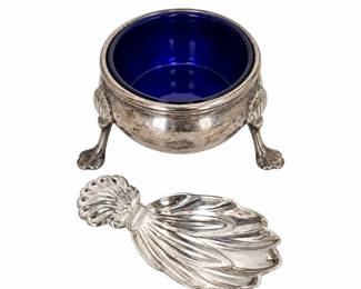 Elegant sterling silver salt cellar accompanied by a decorative sterling silver shell-form salt spoon. The round cellar features a removable deep cobalt blue glass liner and an ornate sterling body raised on three decorative feet. Accompanied by a substantial sterling silver spoon with an elaborate sculptural shell-form bowl and coordinating shell motif handle. Both silver pieces are marked sterling. The combination of cobalt glass and sterling silver creates a striking presentation suitable for table service, display, or a collection of antique and vintage silver. Sterling surfaces exhibit tarnish, patina, scratches, and age-related wear as shown. Please review photographs for marks, condition, and details.
