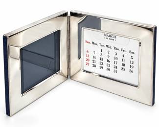Elegant silverplate perpetual desk calendar and photo frame featuring a hinged folding design with polished silver-tone surfaces. One side accommodates a photograph, while the opposite side holds a perpetual calendar with interchangeable monthly and date cards for continued year-to-year use. The compact folding format allows the piece to stand open for display on a desk, vanity, bookshelf, or bedside table and close for convenient storage. A handsome and functional decorative accessory with classic styling. Silverplate surface shows light age-related wear, tarnish, scratches, and/or surface marks consistent with previous use; please review photographs for condition and details.