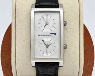 British Airways dual time zone wristwatch featuring a distinctive elongated rectangular curved case with two independently adjustable analog dials, allowing two time zones to be displayed simultaneously. Silver-tone dial and polished silver-tone case are accented by the British Airways name and logo. Fitted with a black leather band and traditional buckle closure. Two separate crowns correspond with the individual time displays. An unusual aviation and travel collectible with a sleek contemporary design. Watch and leather band show visible signs of previous use, including surface wear, scratches, and wear to the strap; please review photographs carefully for condition. Working condition and timekeeping accuracy have not been verified unless otherwise stated. Sold as pictured.