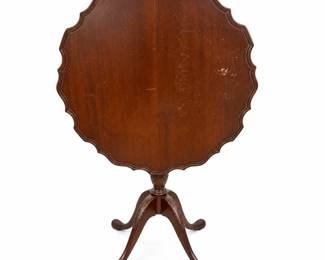 Vintage mahogany tilt-top occasional table featuring a decorative pie-crust scalloped edge, molded tabletop, carved central pedestal and three gracefully curved tripod legs with carved foliate detailing. The tabletop measures approximately 26 inches across and the table stands approximately 29 inches high when positioned for use. Traditional tilt-top construction allows the tabletop to be raised vertically for display or compact storage. Rich dark mahogany-tone finish with attractive traditional styling suitable as an accent, occasional, tea or side table. Vintage pre-owned condition with visible surface scratches, scuffs, finish wear and marks to the tabletop and other areas consistent with age and use; condition has intentionally not been restored or concealed. Please review all photographs carefully for construction, measurements and condition details.