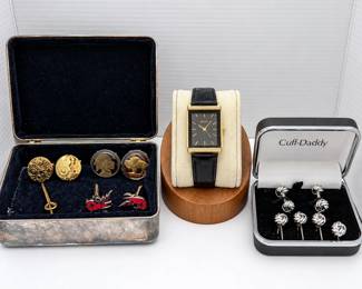 Men’s accessory collection featuring a Pulsar rectangular wristwatch with black dial, gold-tone case, gold-tone hour markers and black leather strap, accompanied by an assortment of decorative cufflinks and accessories. Collection includes silver-tone knot-style cufflinks presented in a Cuff-Daddy box, watch-movement/steampunk-style cufflinks, buffalo and Native American coin-style cufflinks, red enamel lobster cufflinks, and additional gold-tone accessory. Also included is a vintage rectangular metal jewelry/cufflink box with dark velvet-lined interior and naturally aged exterior patina. Watch and accessories show varying signs of previous use and age. Watch functionality and accuracy have not been independently verified unless otherwise noted. Please review all photographs carefully for design, included pieces, condition and additional details.