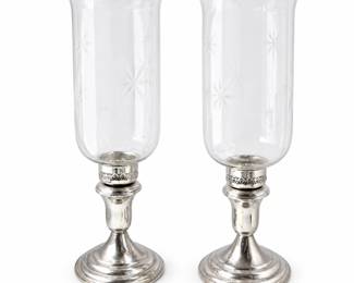 Elegant pair of weighted sterling silver candlesticks featuring polished stepped circular bases, classic tapered stems, and pierced candle cups, each fitted with a tall clear glass hurricane shade. The hurricane shades are beautifully decorated with delicate etched starburst, floral and geometric motifs and feature gently flared rims. A timeless decorative pair suitable for dining tables, mantels, buffets or traditional interiors. Sterling bases show age-appropriate surface wear, tarnish and light scratching consistent with use. Glass appears in good overall condition with no obvious major chips or cracks visible in photographs. Please review all photographs carefully as they are considered part of the condition description. Condition Report Ordinary wear for an item of this age and use.