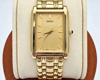 Vintage Seiko quartz dress wristwatch featuring an elegant rectangular gold-tone case, champagne-gold dial, applied baton hour markers, and textured basket-weave style center dial. The watch is fitted with a coordinating gold-tone multi-link Seiko bracelet and clasp. Case back is marked “SEIKO WATER RESISTANT ST. STEEL + BASE METAL V701-5E49 R1 MOV’T JAPAN” with serial number 893281. Bracelet clasp is marked “SEIKO STAINLESS STEEL-B BAND CHINA.” Approximately eight inches in overall length as photographed with ruler. Pre-owned vintage condition with surface wear, scratches, and signs of use consistent with age; please review all photographs for condition and details. Functionality and accuracy have not been independently verified unless otherwise stated. Sold as photographed.