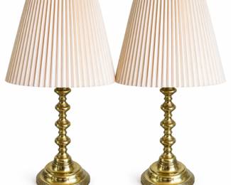 Elegant matching pair of vintage brass table lamps featuring tall turned candlestick-form bodies with repeating baluster details, substantial stepped circular bases, and decorative rope-twist ring finials. Each lamp is fitted with a classic pleated light cream shade, creating a traditional and versatile look suitable for bedside tables, living rooms, libraries, or formal interiors. Brass surfaces display attractive age-related patina, oxidation, spotting, and surface wear consistent with previous use, as shown in the photographs. Shades show light signs of use. Electrical components and working condition have not been independently verified. Maker and exact age have not been identified. Please review all photographs carefully for design, finish, and condition. Sold as a matching pair.