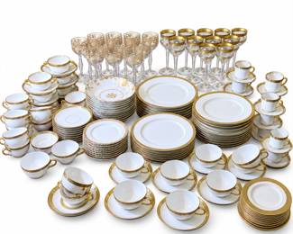 Extensive coordinated collection of elegant white fine china and crystal tableware featuring richly decorated gold-tone borders and accents. This impressive assortment includes multiple sizes and styles of dinner plates, luncheon and dessert plates, bowls, teacups and saucers, demitasse cups and saucers, serving pieces, and coordinating crystal stemware with ornate gold decoration. The collection appears to include multiple complementary patterns unified by classic white and gold styling, making it ideal for formal dining, holiday entertaining, weddings, special occasions, or mixing and matching with an existing gold-trimmed service. Offered together as one large collection with all pieces shown included. Pre-owned condition with expected signs of previous use; individual pieces may exhibit light surface wear, utensil marks, or wear to gold decoration. Please review photographs carefully for exact contents, patterns, condition, and quantities.