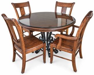 Traditional round dining set featuring a 46-inch diameter table with a removable glass top, warm wood finish, and decorative dark metal scrollwork pedestal base. Table includes one 15-inch extension leaf, allowing the table to expand to approximately 61 inches long when installed. Accompanied by four coordinating wood dining chairs, including armchairs and side chairs, with shaped backs and wood seats. Chairs show age and use, including surface scratches, scuffs, finish wear, and other marks consistent with previous use. Please review photographs carefully for construction and condition. Maker and wood species have not been independently identified. Sold as a complete dining set with table, one extension leaf, and four chairs.
