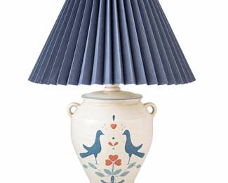 Charming vintage table lamp fashioned in the style of a traditional stoneware crock, featuring an ivory speckled ceramic body with applied side handles and hand-painted folk art decoration. The design depicts a pair of stylized blue birds facing one another above a floral motif with muted red, blue and blue-green accents, complemented by coordinating blue trim at the base and shoulder. Finished with a dramatic navy blue accordion-pleated shade that gives the lamp a classic country, Americana and cottage-inspired appearance. Pre-owned vintage condition with expected signs of age and use; please review photographs carefully for condition, decorative details and components included.