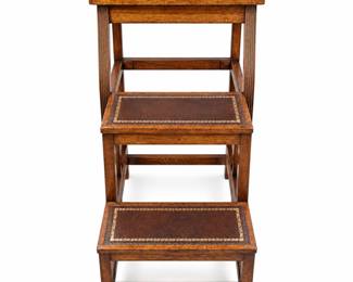Traditional three-step library table stool featuring a dark wood frame with three graduated steps and a useful tabletop-height upper surface. Each level is fitted with a rich brown leather-style inset accented by an elegant gilt-tooled foliate border, complemented by reeded vertical supports and stretcher construction. Designed in the classic library-step tradition, the piece combines decorative appeal with a compact architectural form suitable for a library, study, office, or traditional interior. Pre-owned condition with visible scratches, scuffs, finish wear, and other signs of age and use, particularly to the inset surfaces and wood edges, as shown in photographs. Exact maker, age, wood species, and inset material have not been independently identified. Please review all photographs carefully for construction, details, and condition. Sold as photographed.