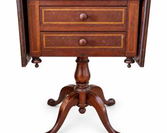 Auction Description: Elegant antique wooden pedestal work or side table featuring a rectangular top with decorative contrasting line inlay, two front drawers with wooden knobs, and hinged drop-leaf side panels that expand the usable surface. The case is supported by a substantial turned central pedestal terminating in four gracefully curved legs. Additional inlaid borders accent the drawer fronts and side panels. A versatile form historically associated with sewing, work, or occasional tables and equally attractive today as an accent or bedside table. Antique condition with visible surface scratches, finish wear, scuffs, spotting, discoloration, and other age-related wear throughout, including wear to the drawer interiors and top as shown. Exact maker, wood species, age, and origin have not been independently identified. Please review photographs carefully for construction and condition. Sold as photographed.