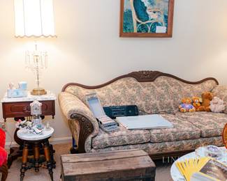 Victorian-style sofa, “By the Sea” print by Renoir, antique flat-top travel trunk, teacups, National Geographic Magazines, antique piano stool with marble top