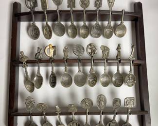 Vintage decorative metal spoons—featuring brands, figures, and advertising logos—displayed on a multi-tiered wooden wall rack.
