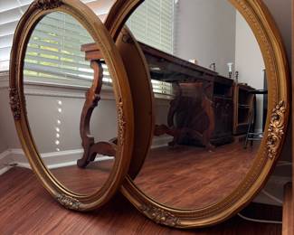 pair of ornate, gold-gilded oval wall mirrors