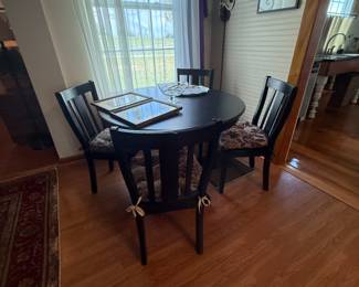 Round black wood dining table with four slat-back chairs