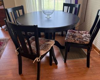 Round black pedestal dining table with four slat-back chairs