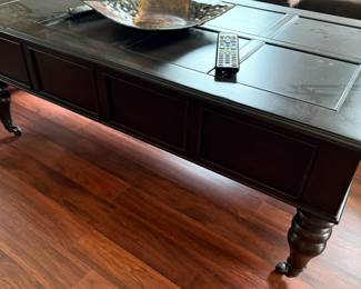 Black wood coffee table with paneled top and turned legs on casters