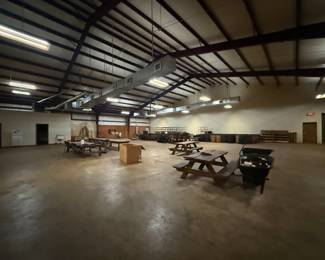 Warehouse view with picnic tables, wheelbarrow, and storage racks