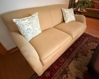 Tan upholstered two-cushion sofa with damask throw pillows