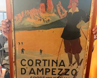 This item is a framed vintage Cortina d'Ampezzo Italian travel poster promoting winter sports ("Sport Invernali") for the 1923–1924 season. Originally designed by artist Carlo Pellegrini for the Italian National Tourist Board (ENIT), it features a stylized woman skier in a red headwrap set against the dramatic backdrop of the snowy Dolomite mountains