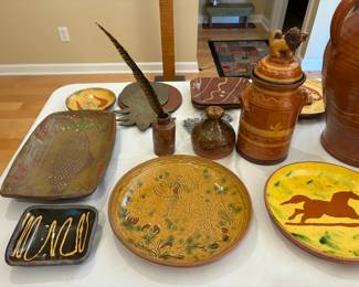 Clockwise from left, redware rectangular fish tray, $100; redware square black and yellow dish, $25; redware plate (center bottom), $55; redware horse plate by Breininger, $50; Redware jar with lion on lid, $185; redware watering bell, $45; redware ink bottle, $30