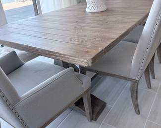 Rustic light-wood dining table with pedestal bases + off-white upholstered chairs with nailhead trim. $1,000