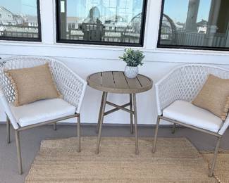 Outdoor bistro set — round slatted table plus 2 white woven-back armchairs with cushions. $400