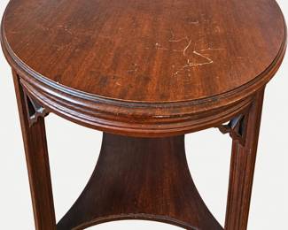 Round wooden side table with decorative brackets, a shaped lower shelf, and visible surface scratches.