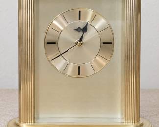 Brass-tone tabletop clock with a round dial, black hour markers, and fluted side columns.