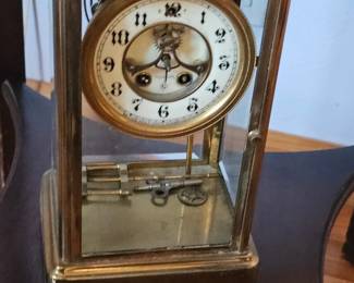 Vintage brass mantel clock with glass panels, an ornate numbered dial, visible pendulum, and winding keys. Shows age and patina.