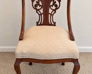 Carved Wood Chair Ornate scrollwork back, curved legs, and a cream patterned upholstered seat.