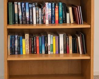 Wood bookcase with open shelves and an assortment of hardcover and paperback books. All books and bookcase are sold separately.