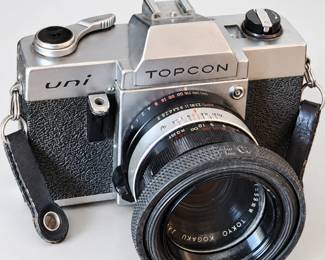 Vintage Topcon Uni film camera with an attached lens, silver-and-black body, and carrying strap.