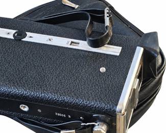 Large vintage folding camera with black textured covering, silver-tone hardware, carrying handle, and fitted case.