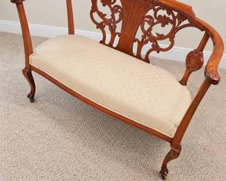 Carved wood settee with ornate scrollwork, curved arms, and a cream patterned upholstered seat.